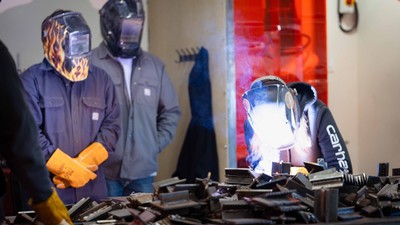 Two people watch a third person giving a welding demonstration